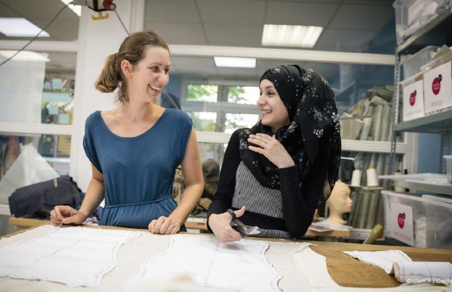 German seamstress helps trainee Syrian refugee at Stitch by Stitch fashion workshop in Frankfurt